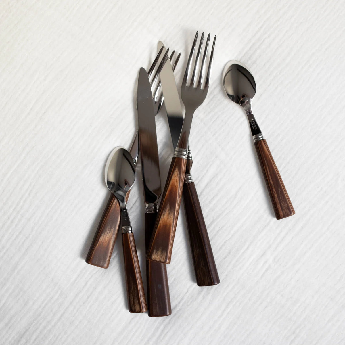 The Sabre Nature Flatware 5 Piece Setting in light wood is arranged on a textured white cloth. This stylish set is dishwasher safe for easy cleaning.
