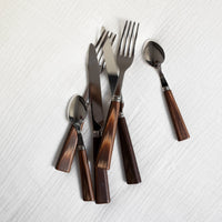 The Sabre Nature Flatware 5 Piece Setting in light wood is arranged on a textured white cloth. This stylish set is dishwasher safe for easy cleaning.
