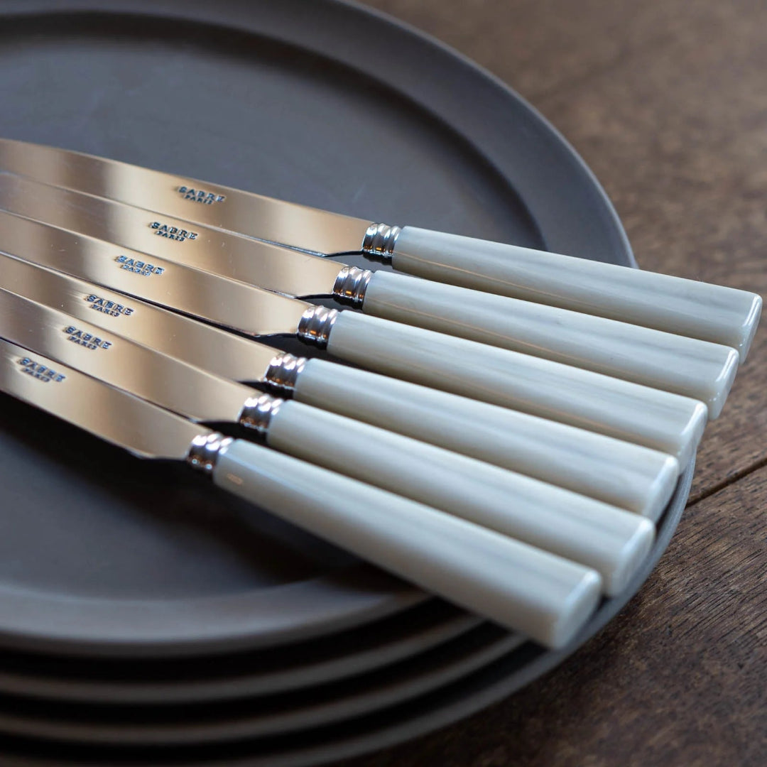 Five-piece Nature Flatware Setting by Sabre, featuring faux horn handles, is arranged atop dark grey plates on a wooden surface with the parallel handles facing outward.