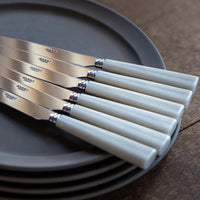 Five-piece Nature Flatware Setting by Sabre, featuring faux horn handles, is arranged atop dark grey plates on a wooden surface with the parallel handles facing outward.