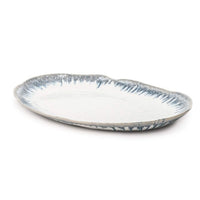 The Simon Pearce Burlington Dinnerware Pool ceramic oval platter features a wavy, glazed edge with a white glaze and blue-gray brushstroke accents—an elegant addition to your pottery or Burlington collection.
