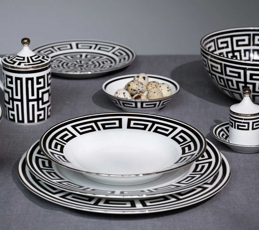 Labirinto Dinnerware Nero by Ginori 1735 features black and white porcelain plates, bowls, cup, saucer, and lidded containers with Gio Ponti-inspired geometric patterns, arranged on a grey tablecloth. One bowl holds quail eggs.