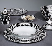 Labirinto Dinnerware Nero by Ginori 1735 features black and white porcelain plates, bowls, cup, saucer, and lidded containers with Gio Ponti-inspired geometric patterns, arranged on a grey tablecloth. One bowl holds quail eggs.