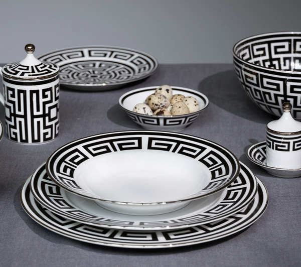 Labirinto Dinnerware Nero by Ginori 1735 features black and white porcelain plates, bowls, cup, saucer, and lidded containers with Gio Ponti-inspired geometric patterns, arranged on a grey tablecloth. One bowl holds quail eggs.