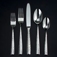 The Ricci Anvil Flatware 5 Piece Setting, crafted from 18/10 stainless steel, includes a salad fork, dinner fork, knife, soup spoon, and teaspoon—each with hammered textured handles and polished surfaces.