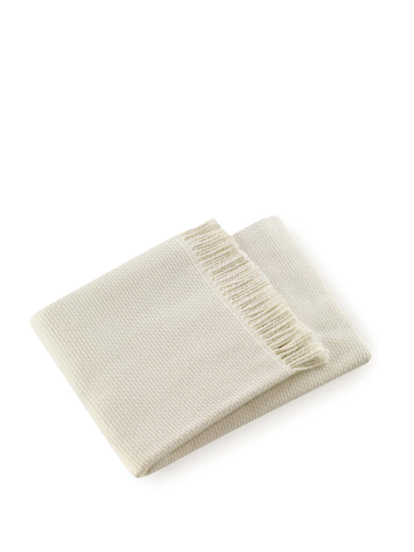 The Grain of Rice Throw by A Soft Idea is a super soft, light beige woven blanket with fringed edges, shown folded on a white background.
