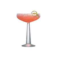 A Big Top Coupe Glass from Nude Glassware’s Set of 2, crafted from lead-free crystal, holds a pink frozen drink with a lime twist garnish, shown against a white background.