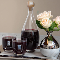 The Elevo DOF Glasses Smoke Set of 2 by Anna New York, filled with red wine, rest on a tray beside a silver vase of pale peach roses.