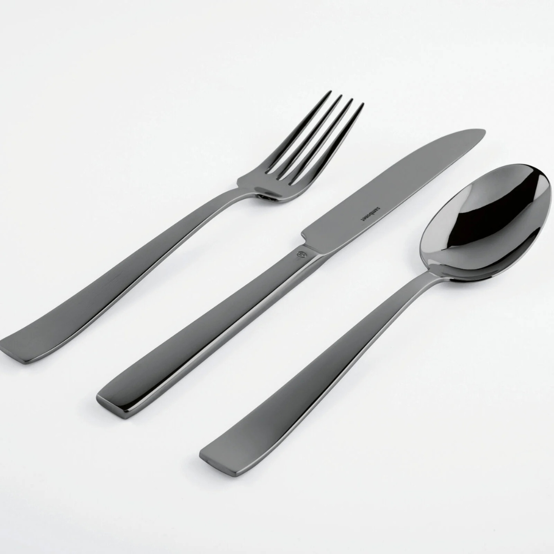 The Sambonet Flat PVD Flatware 5 Piece Setting in Black showcases a knife, fork, and spoon with modern, sleek lines and smooth, slightly curved handles—all arranged side by side against a white background.