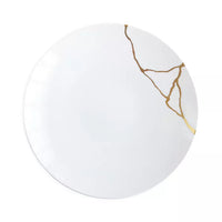 A white plate featuring a gold crack-like design along one edge, the Kintsugi Dinnerware by Bernardaud beautifully exemplifies the refined craftsmanship of Limoges, France and draws inspiration from the Japanese art of kintsugi.