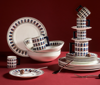 The Palazzo Navy Dinnerware 3 Piece Set by Greg Natale features blue and red arch patterns on fine bone china plates, bowls, and cups, elegantly displayed with cutlery and chocolate balls.