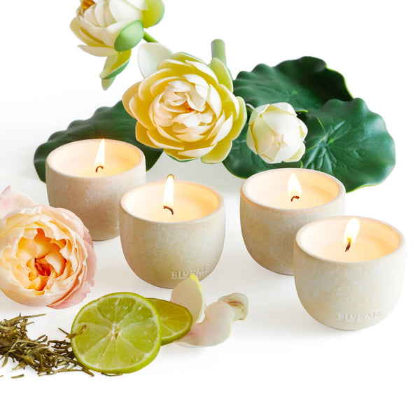 The Blueme Travel Votive 4 Piece Set—Romance, Spiritual, Happiness, Renew—features lit soy wax candles in handcrafted ceramic holders with floral accents, lime slices, and tea leaves on a white background.