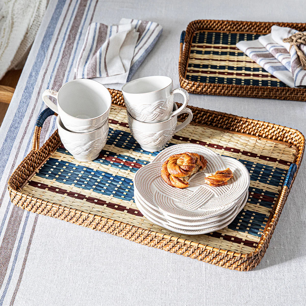 The Juliska Danish Stripe Serving Tray Navy 21" holds stacked white plates, two pastries, and cups on a linen tablecloth with blue-striped napkins, showcasing Scandinavian-inspired design.
