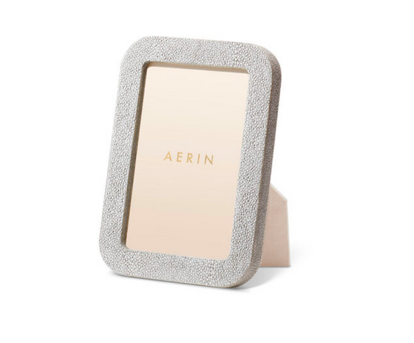 The Modern Shagreen Frame Dove by Aerin features a textured light gray embossed shagreen in a rectangular shape, standing upright on a white background, with "AERIN" in gold displayed on the placeholder inside the frame.
