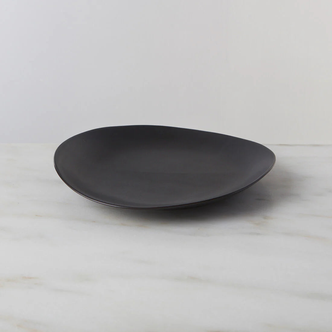 The Barre Dinnerware Slate plate by Simon Pearce, in matte black stoneware, rests on white marble with a light gray backdrop—an elegant example of modern dinnerware handcrafted in the USA.