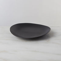 The Barre Dinnerware Slate plate by Simon Pearce, in matte black stoneware, rests on white marble with a light gray backdrop—an elegant example of modern dinnerware handcrafted in the USA.