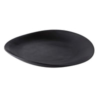 The Simon Pearce Barre Dinnerware Slate is a black, asymmetrical stoneware plate with a smooth matte finish, shown on a white background as part of their modern dinnerware set.