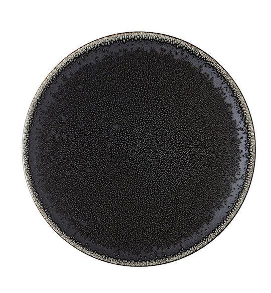 The Tourron Dinnerware Celeste by Jars - Rosenthal is a round, black glazed stoneware plate with a speckled texture and lighter rim, shown from above on a white background. This artisanal ceramic piece is stylish and dishwasher safe.