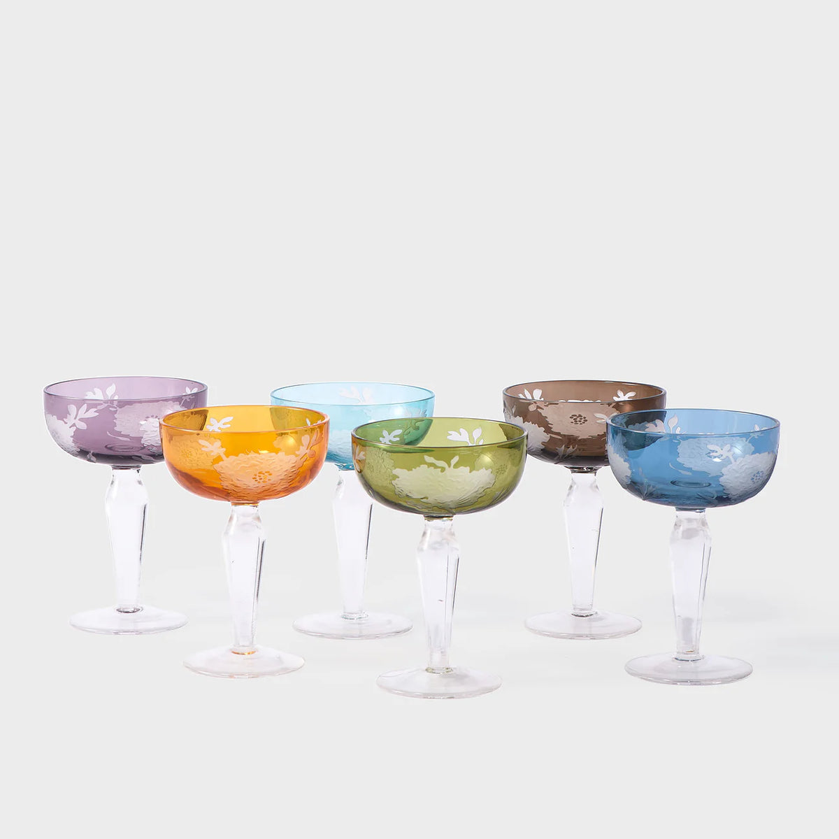 The Peony Coupe Glass Multi Set of 6 by Polspotten features six colored glass goblets, each in a different shade with clear stems and a sandblasted pattern, adding texture and charm against a plain background.