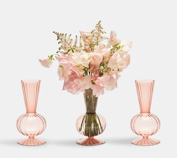 Three light pink, fluted, hand-blown glass Tess Bud Vase Set of 3 - Blush, one filled with a bouquet of pale pink flowers.