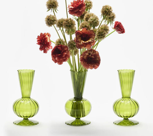 The Tess Bud Vase Set of 3 - Olive by Kim Seybert features ribbed, rounded green glass vases. The center vase displays red and cream flowers with green stems, while the two side vases remain empty.