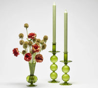 The Tess Bud Vase Set of 3 - Olive by Kim Seybert, featuring hand-blown green glass, is displayed with two matching candle holders and light green candles against a plain white background.