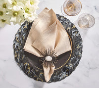 Elegant table setting with a black and gold marbled plate, beige napkin held by the Kim Seybert Flare Napkin Ring Black & Gold Set of 4, two gold-rimmed glasses, and a bouquet of white flowers on the side.