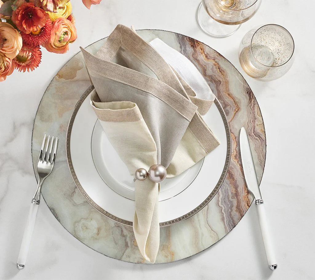 Elegant table setting featuring Kim Seybert’s Pearl Napkin Ring Grey & Silver Set of 4, marble-patterned charger plate, white china, beige and white napkins, silverware, two glasses, and orange flowers—perfect for sophisticated wedding decor.