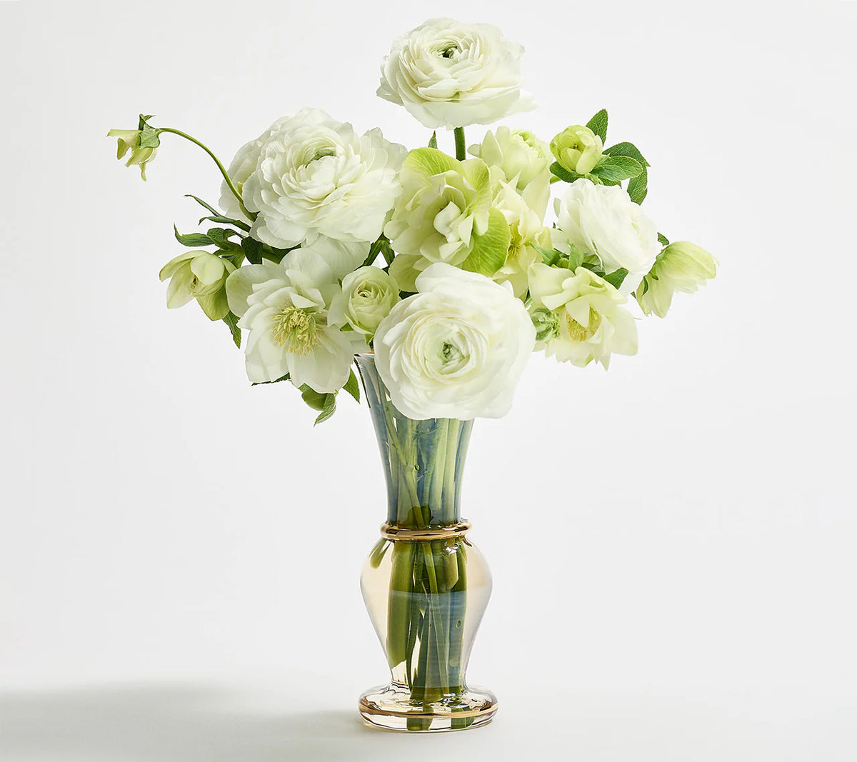 The Kim Seybert Champagne Rib Gold Detail Vase, made from clear mouth-blown glass, is shown filled with white and pale green roses and ranunculus against a plain white background.
