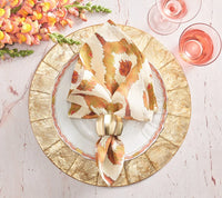 Elegant table setting with gold-rimmed plates, a patterned napkin held by the Kim Seybert Desert Napkin Ring Gold & Silver, pink flowers to the side, and two glasses of pink drink on a pale marble surface.