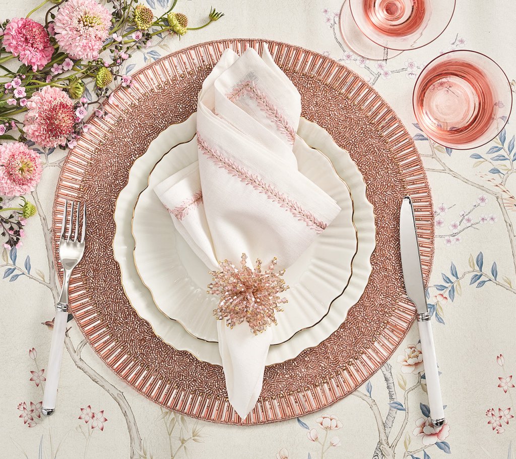 Elegant table setting featuring Kim Seybert’s Jardin Napkin Set of 4, layered pink and white plates, sparkling napkin ring, silver cutlery, pink wine glasses, and pink florals on a floral-patterned tablecloth.