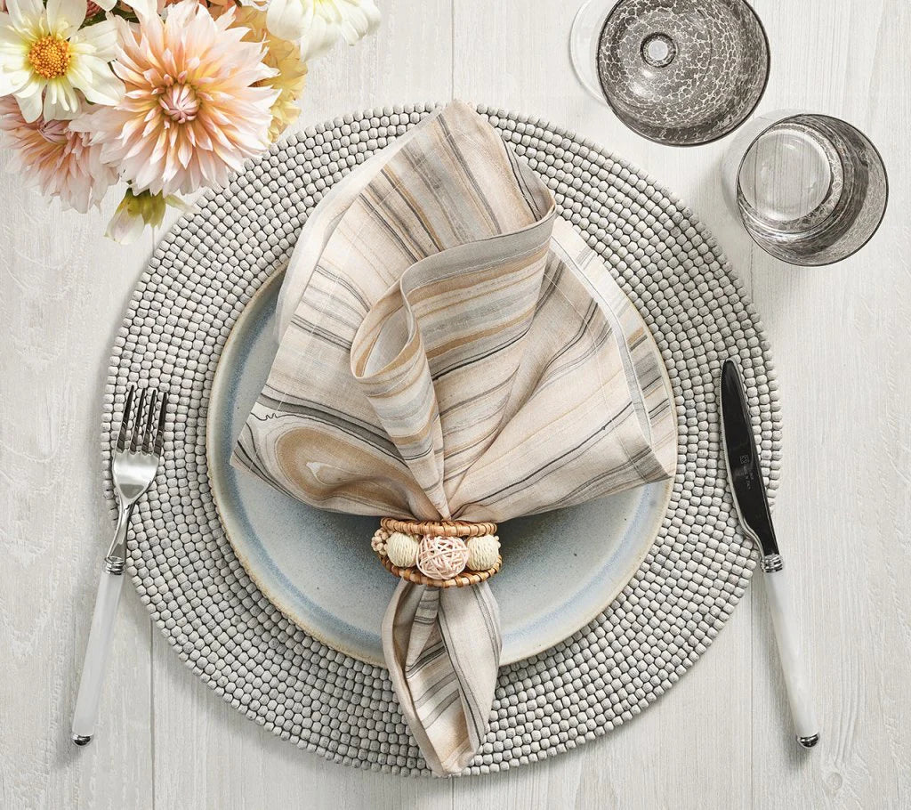A table set with Kim Seybert Driftwood Placemat Set 4 Grey, ceramic plate, striped napkin in a ring, silverware, two gray glasses, and a bouquet of pale pink and white flowers for a handcrafted decor touch.
