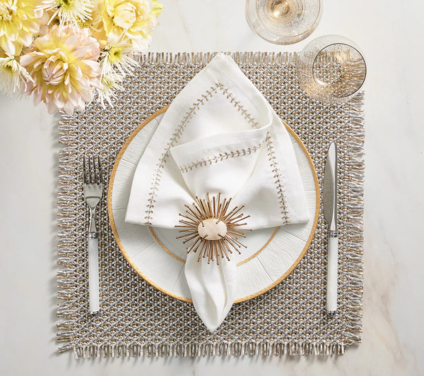 Elegant table setting featuring a white plate with gold rim, white stitched napkin with Kim Seybert Flare Napkin Ring Gold, silverware, wine glass, yellow flowers in the corner, all atop a textured placemat.