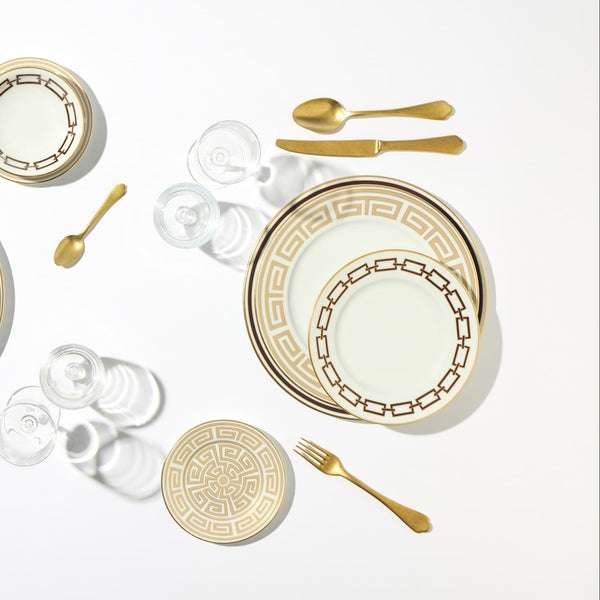 A formal table setting with Ginori 1735 Catene Cachemire Beige dinnerware, gold flatware, and clear glassware. Includes a dinner plate, salad plate, bread plate, and cups on a white background.