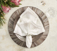 A formal table features a patterned charger, metallic plate, and white napkin with silver dots in silver rings. Two glasses sit on the elegant Kim Seybert Aura Placemat Grey Set of 4, alongside a bouquet of pink flowers.