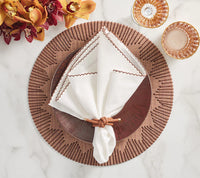 A table setting with a set of 4 Kim Seybert Dream Weaver brown placemats, a dark brown plate, white napkin with brown trim in a braided ring, two pink glass cups, and yellow and burgundy flowers.