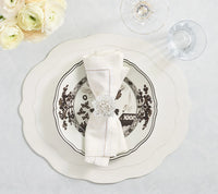 A stylish tablescape featuring the Kim Seybert Tailored Placemat s/4 in White as a base, topped with a white floral plate, complemented by a cream napkin in a jeweled ring, water glass, wine glass, and a bouquet of white flowers on a light table.