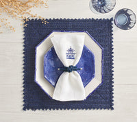 A Kim Seybert Vista Reversible Placemat in Navy & Periwinkle is topped with white and blue octagonal plates, plus a white napkin with a blue pagoda motif in a blue ring; two blue glasses sit nearby.