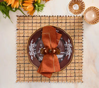 A square, brown Boucle Reversible Placemat set of 4 featuring a plate topped with a folded napkin and ring, set on a table with glassware and flowers for stylish table decor.