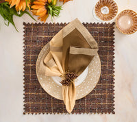 A square brown Boucle Reversible Placemat set of 4 - Brown / Multi with jagged edges, topped with a white-and-gold dotted plate and a folded cream and brown napkin held by a pinecone napkin ring.