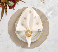 Elevate your dining experience with the Kim Seybert Divot Placemat Set of 4 in Grey as the foundation for an elegant table setting. A decorative plate sits atop the contemporary placemat, accompanied by a white napkin adorned with gold floral patterns and secured by a gold napkin ring. Wine glasses and a refined floral arrangement complete the sophisticated look with these stunning dining room accessories.