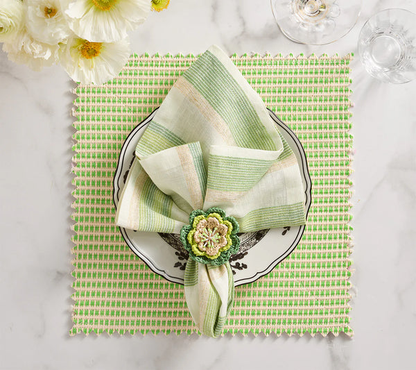 A green and white striped napkin with a floral ring rests on a decorative plate atop the Kim Seybert Duet Placemat Set of 4 - Blue & Green. White flowers and glassware add elegance to these sophisticated table settings on marble.