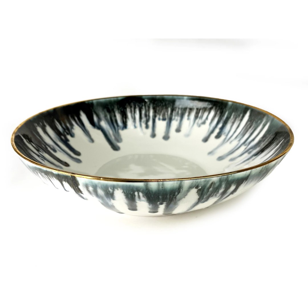 The Michael Wainwright Fjord Serving Bowl - Large is a ceramic bowl with a glossy finish, featuring dark blue and gray drip patterns on the rim and a thin golden edge—an elegant touch for your table setting.