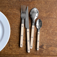The Sabre Bistrot Pearly 5 Piece Setting - Shiny, featuring beige handles and silver rivets, is arranged on a wooden table beside a white plate.