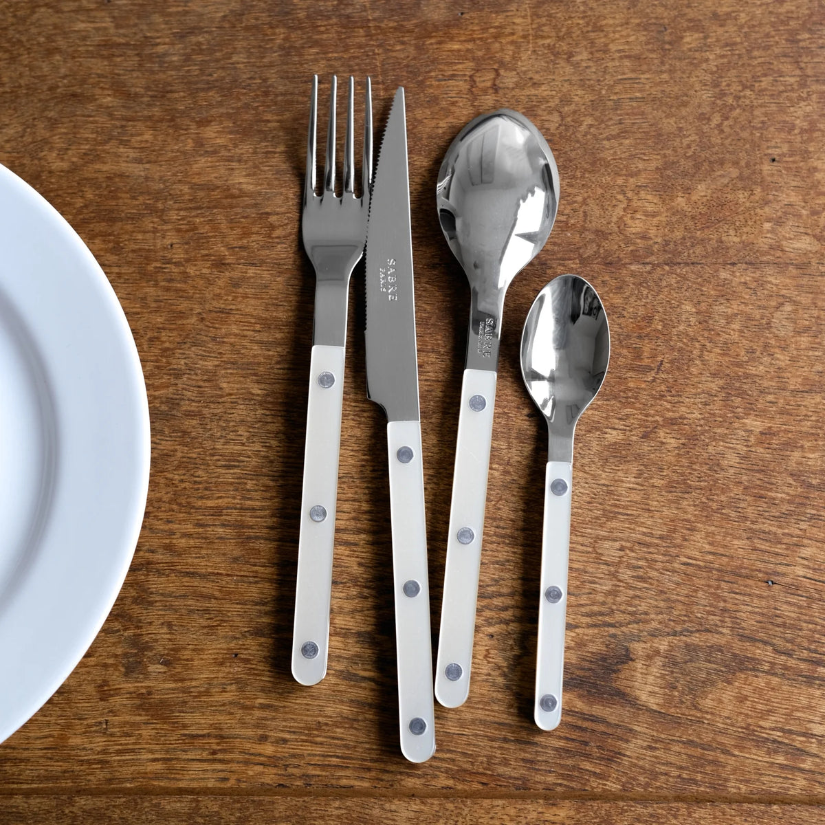 A Sabre Bistrot Pearly 5 Piece Setting - Shiny with white mother of pearl handles and metal rivets is neatly arranged on a wooden table next to a white plate.