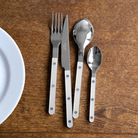 A Sabre Bistrot Pearly 5 Piece Setting - Shiny with white mother of pearl handles and metal rivets is neatly arranged on a wooden table next to a white plate.