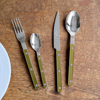 The Sabre Bistrot Pearly 5 Piece Setting - Shiny, with silver heads and green mother of pearl handles, is arranged on a wooden table. A white plate's edge appears in the lower left corner.