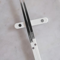 Two Bistrot Solid Chopsticks by Sabre with white handles rest on a white chopstick holder atop a light marble surface, illustrating the refined elegance and the fusion of French craftsmanship with classic Asian tableware.