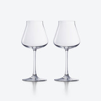 Two empty, clear Chateau Barware wine glasses by Baccarat, featuring wide bowls and slender stems, are placed side by side on a plain, light gray background.