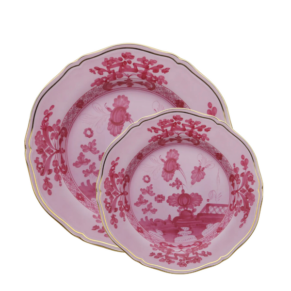 Two pink Ginori 1735 Oriente Italiano Porpora porcelain plates with scalloped gold rims and chinoiserie floral patterns, the smaller plate overlapped atop the larger for an elegant display.